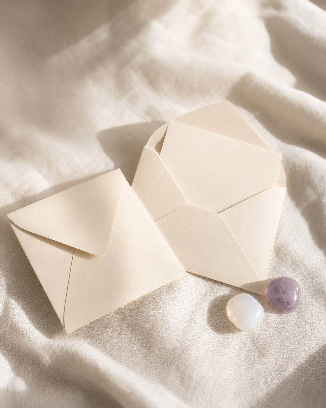 Two cream envelopes and two small stones on warm ivory linen